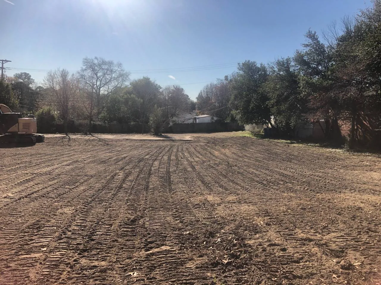 Freshly graded lot with machine track lines across the dirt and trees along the far edge