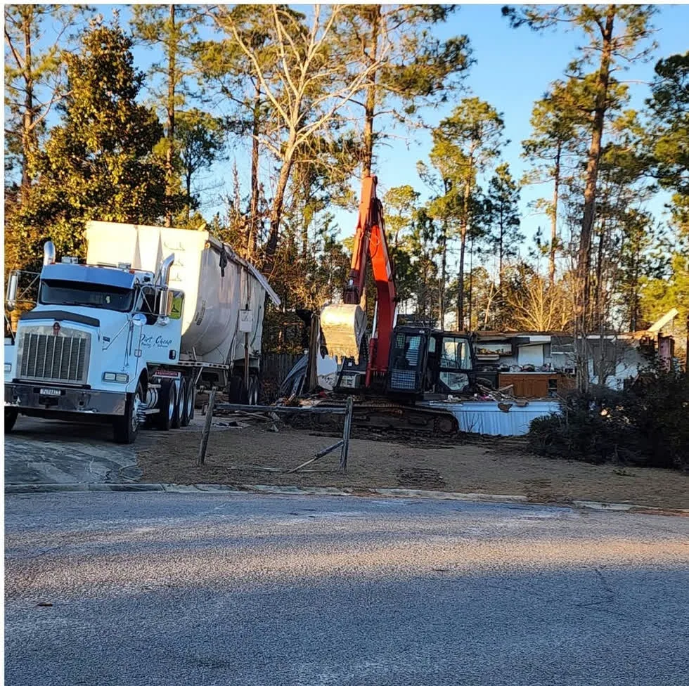 Kenworth dump truck and an excavator tearing down a mobile home on a wooded lot